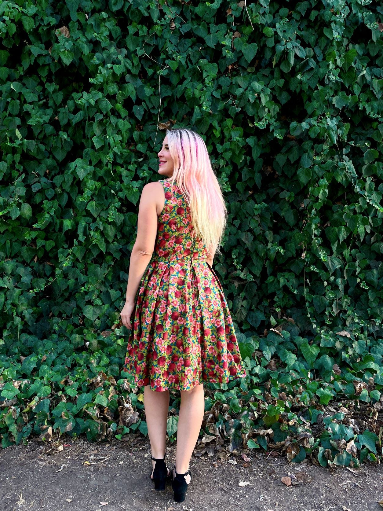 a full length image of the back of a model standing in front of leafy backdrop wearing the Elizabeth dress in pomegranate