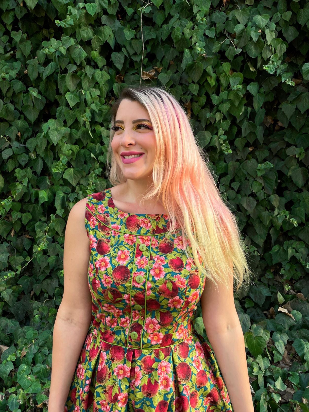 a close up image of a model standing in front of leafy backdrop wearing the Elizabeth dress in pomegranate