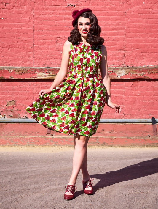 a full size image of a model standing in front a red wall wearing the Elizabeth dress in grapes