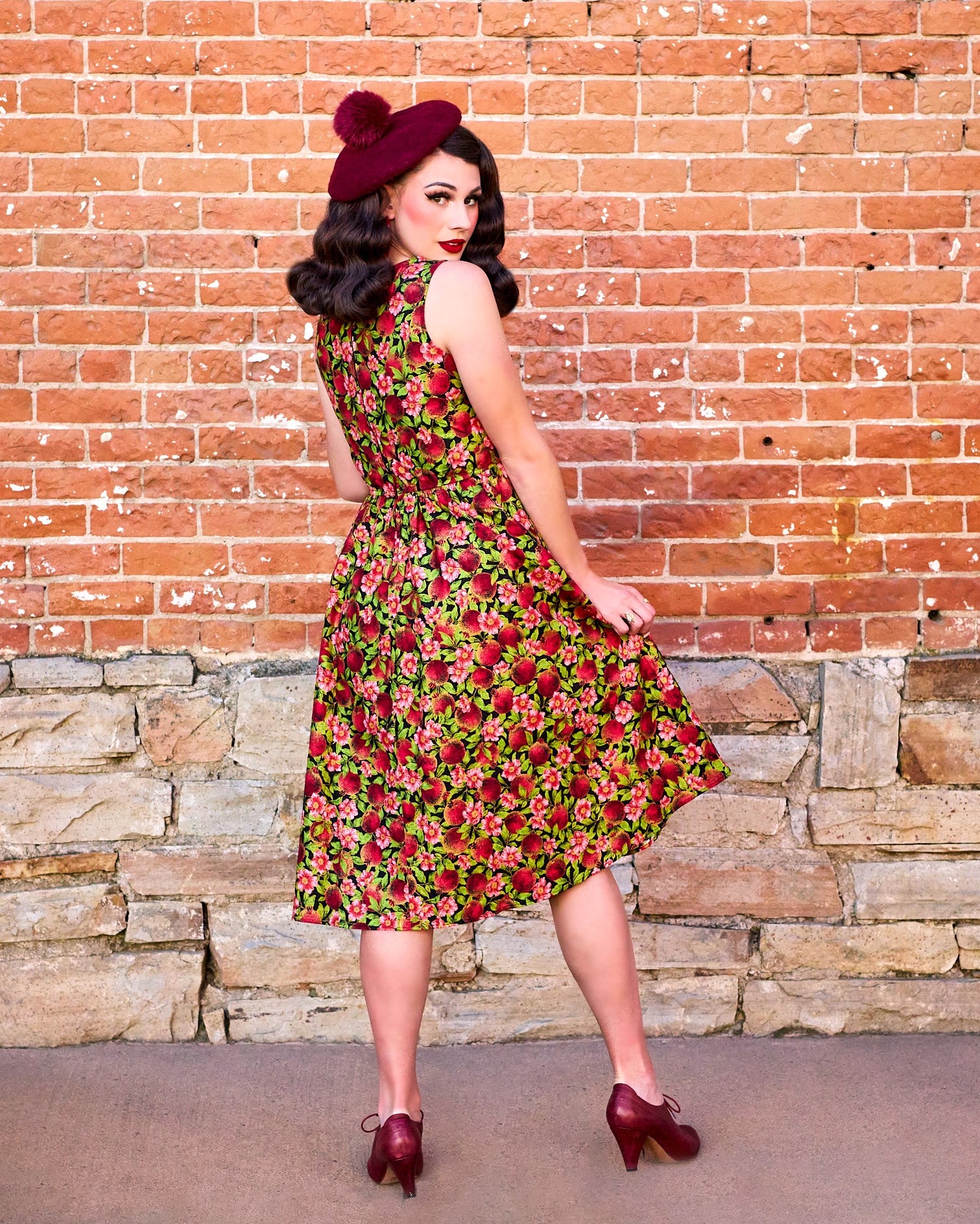 a full length image of the back side of a model standing in front of a brick wall wearing the Pomegranate Midi dress