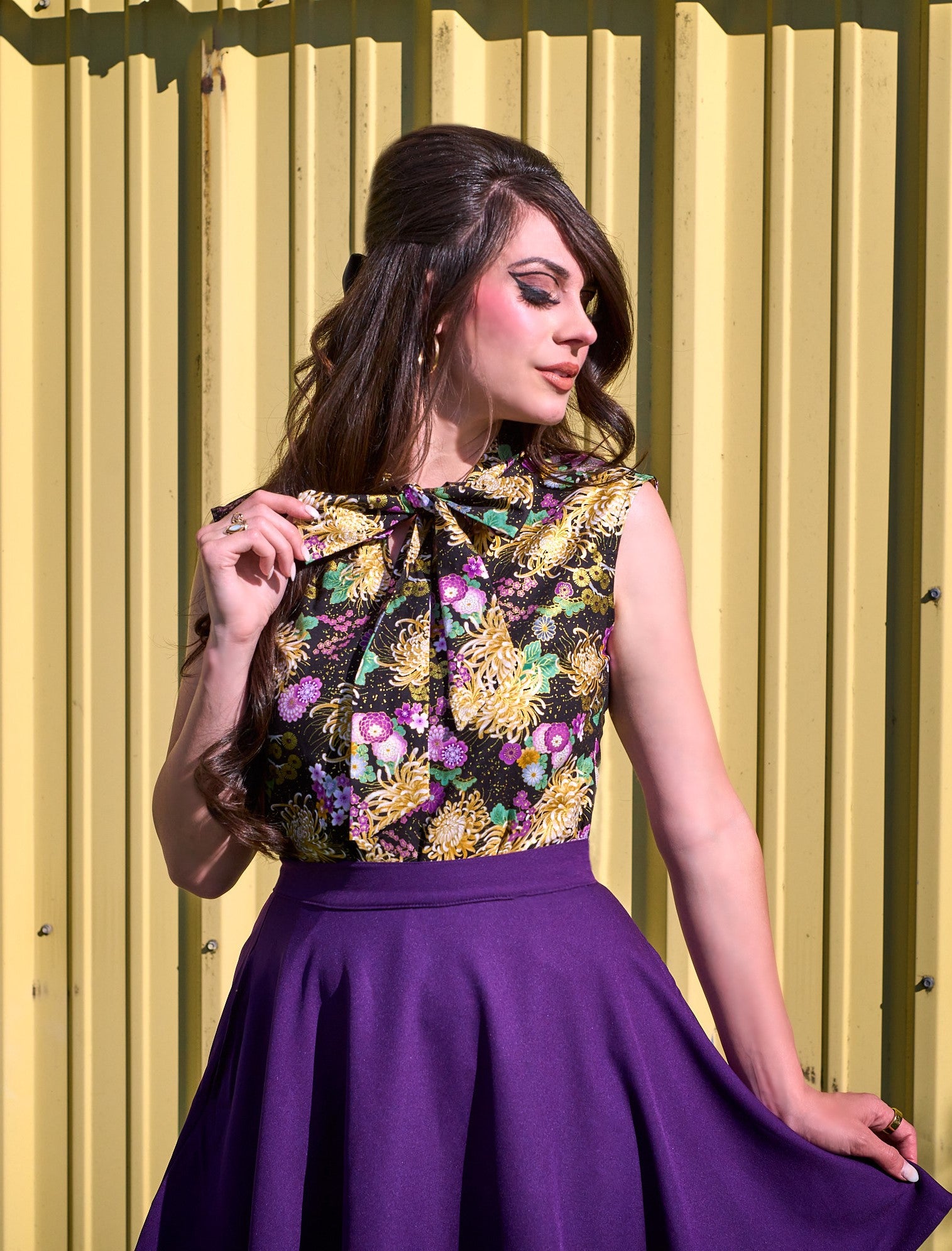 a close up of model standing in front of yellow metal wall wearing the purple skater skirt