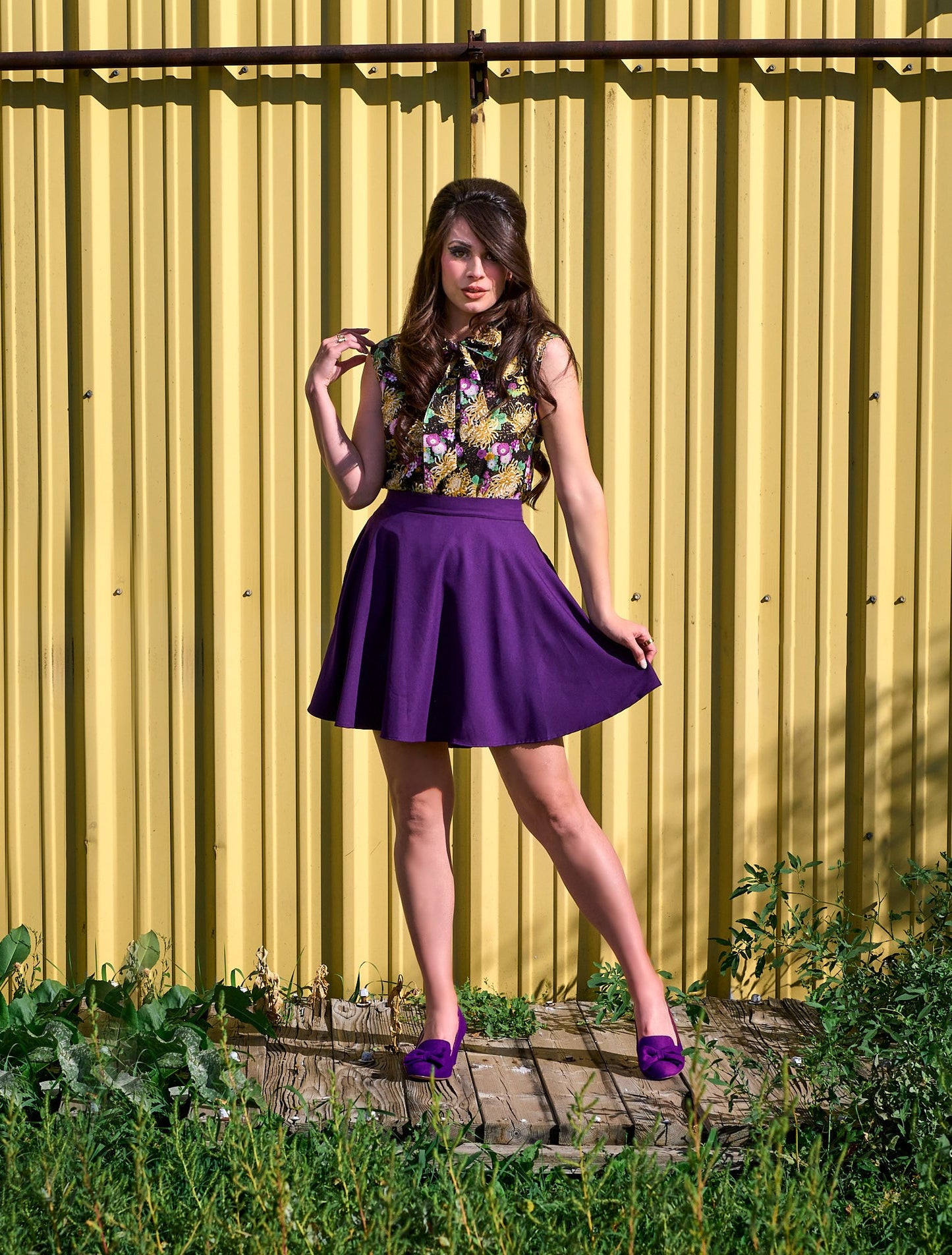 a model standing in front of yellow metal wall wearing the purple skater skirt