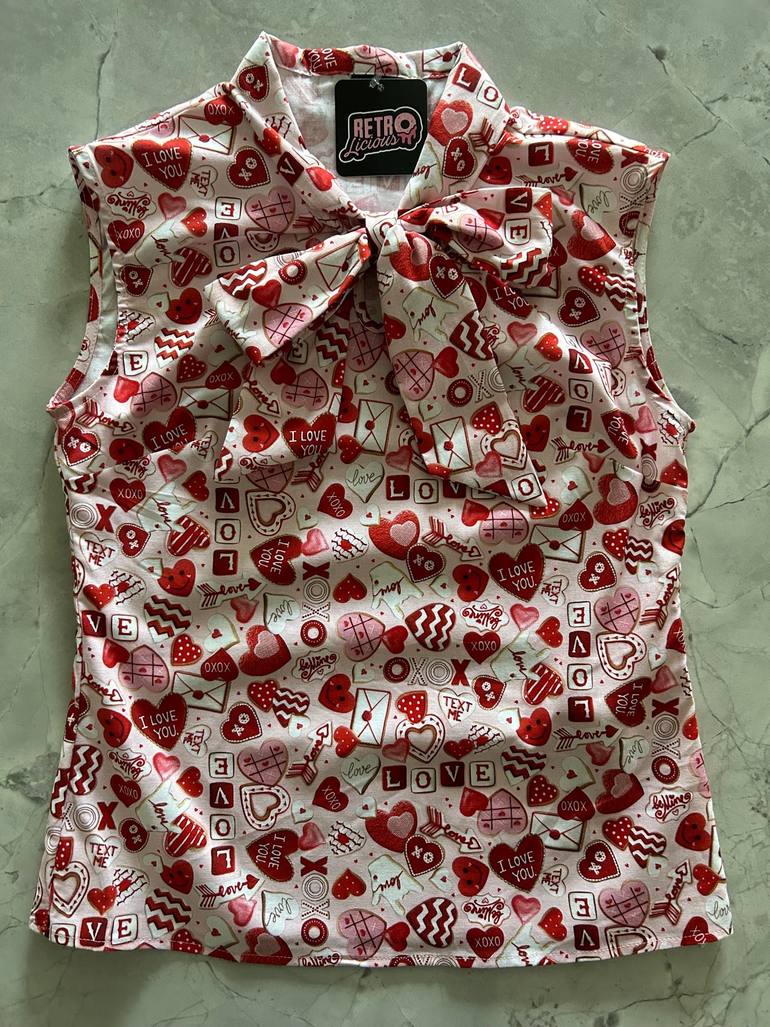 a flat lay of our sleeveless bow tie blouse with xoxo hearts and love fabric