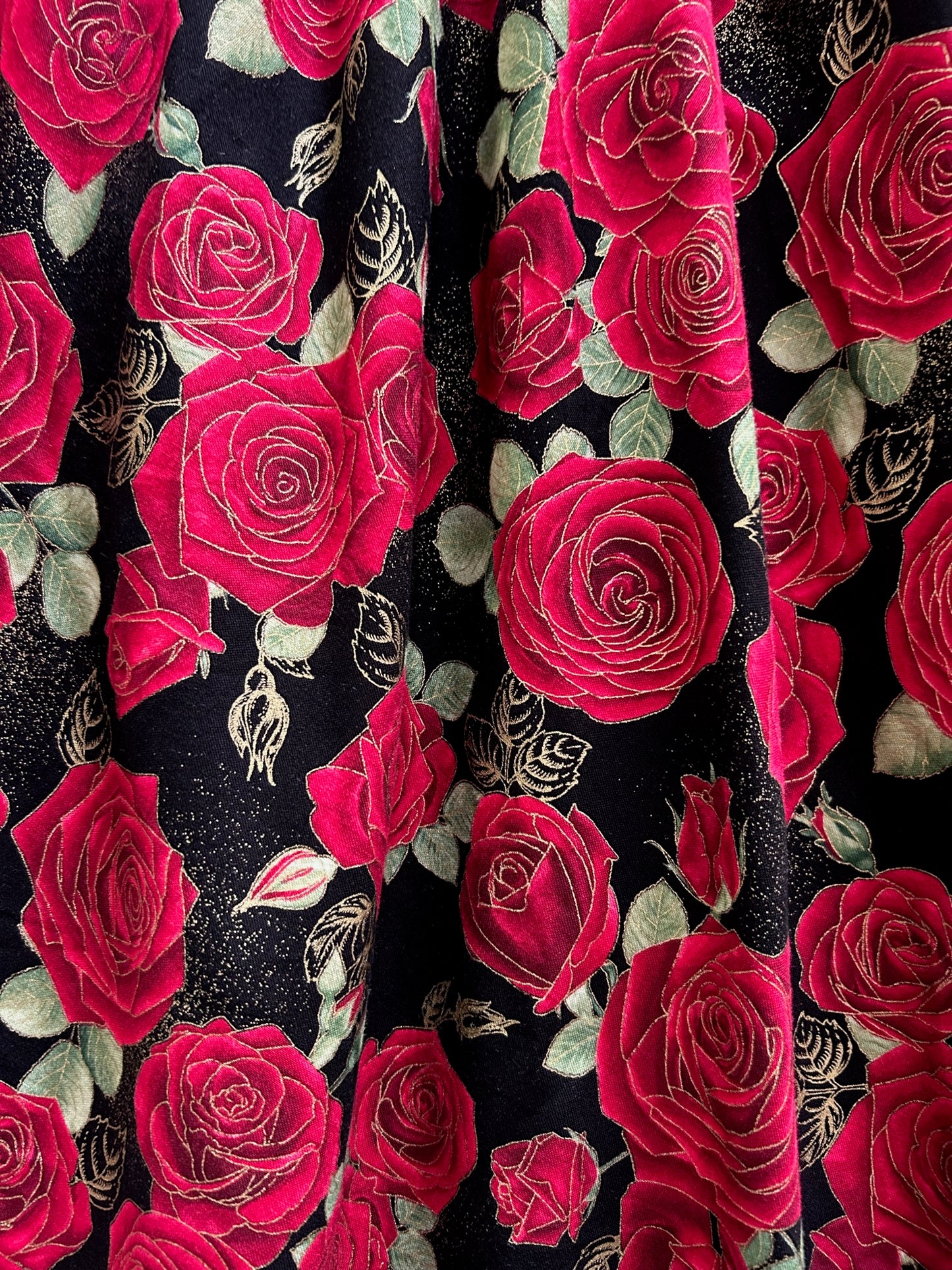 a close up of the fabric showing the red roses on black background and the gold metallic accents