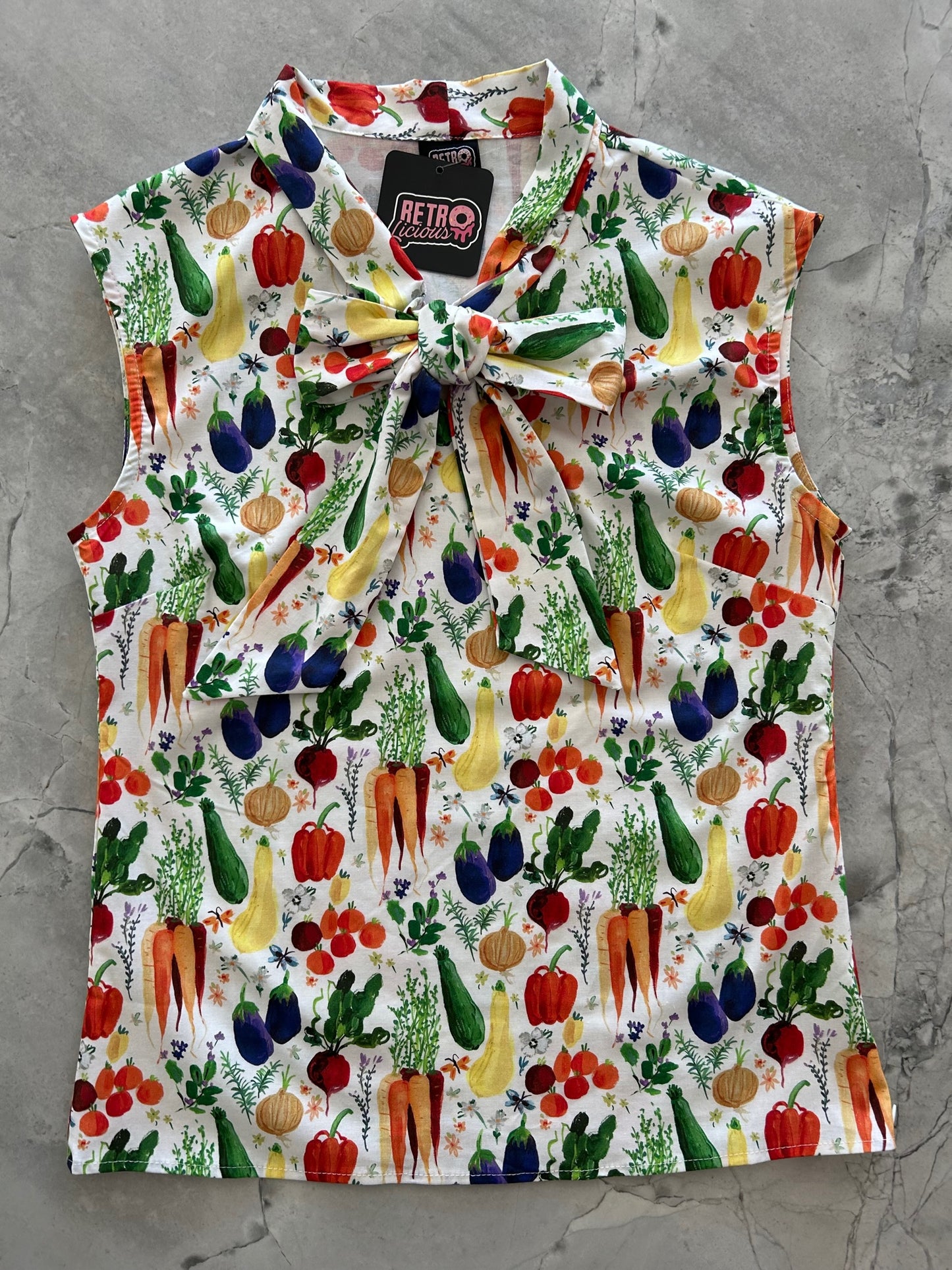 a flat lay of our bow tie blouse in farm to table fabric with carrots, zucchini, pepper and other veggies