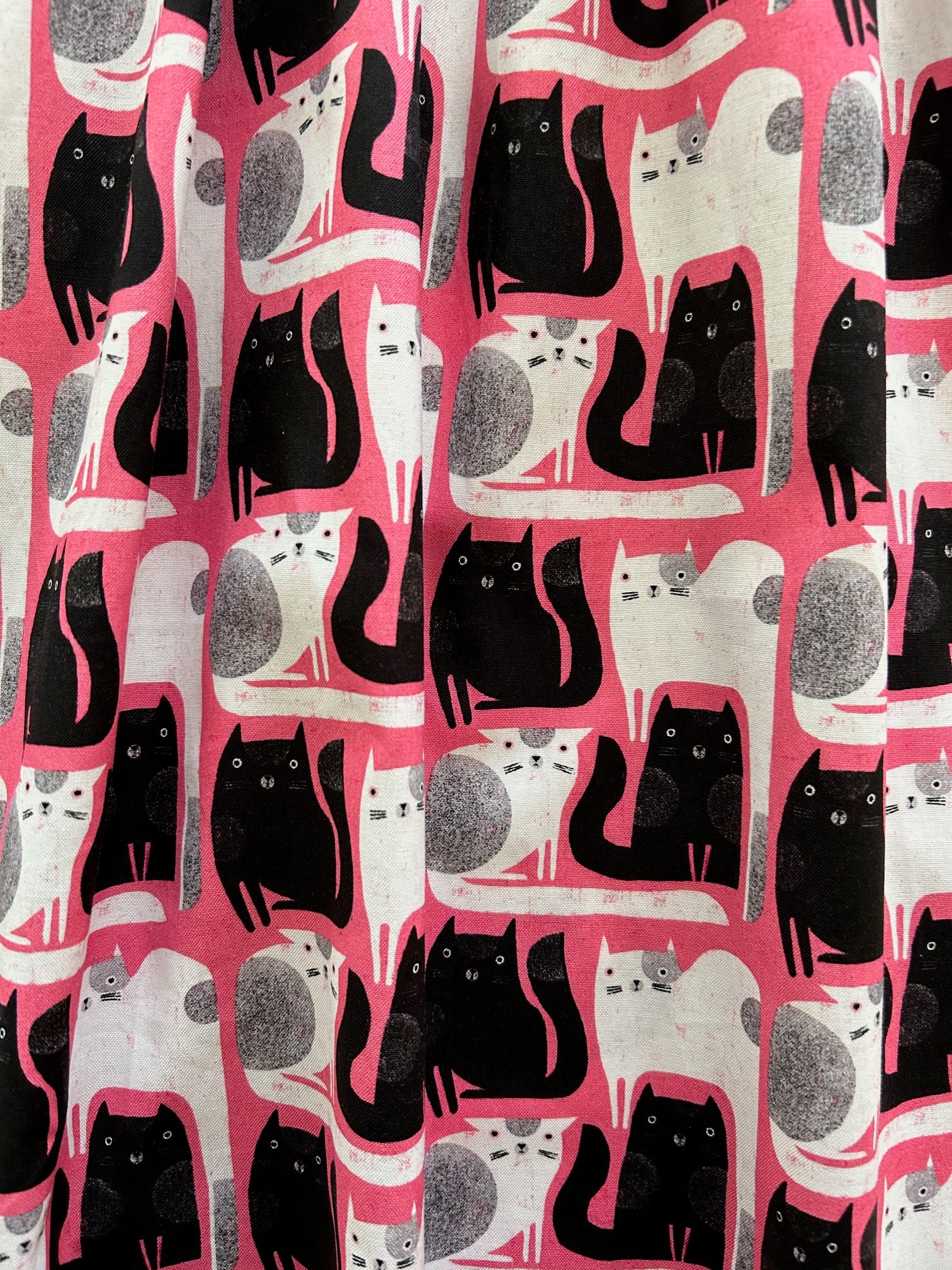 a close up of the fabric showing black and white cats on pink background
