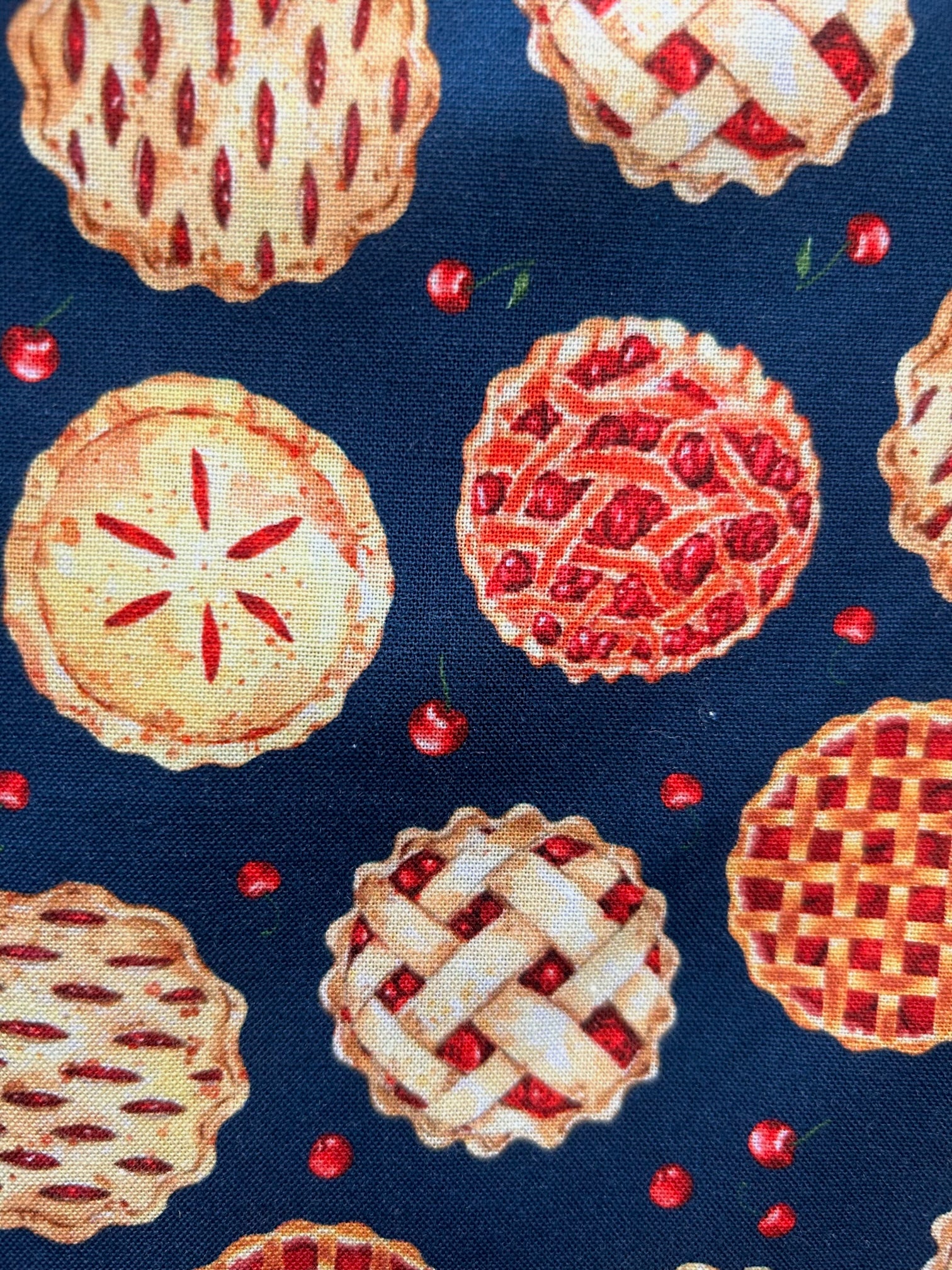 a close up of fabric showing cherry pies and cherries all over print on navy background