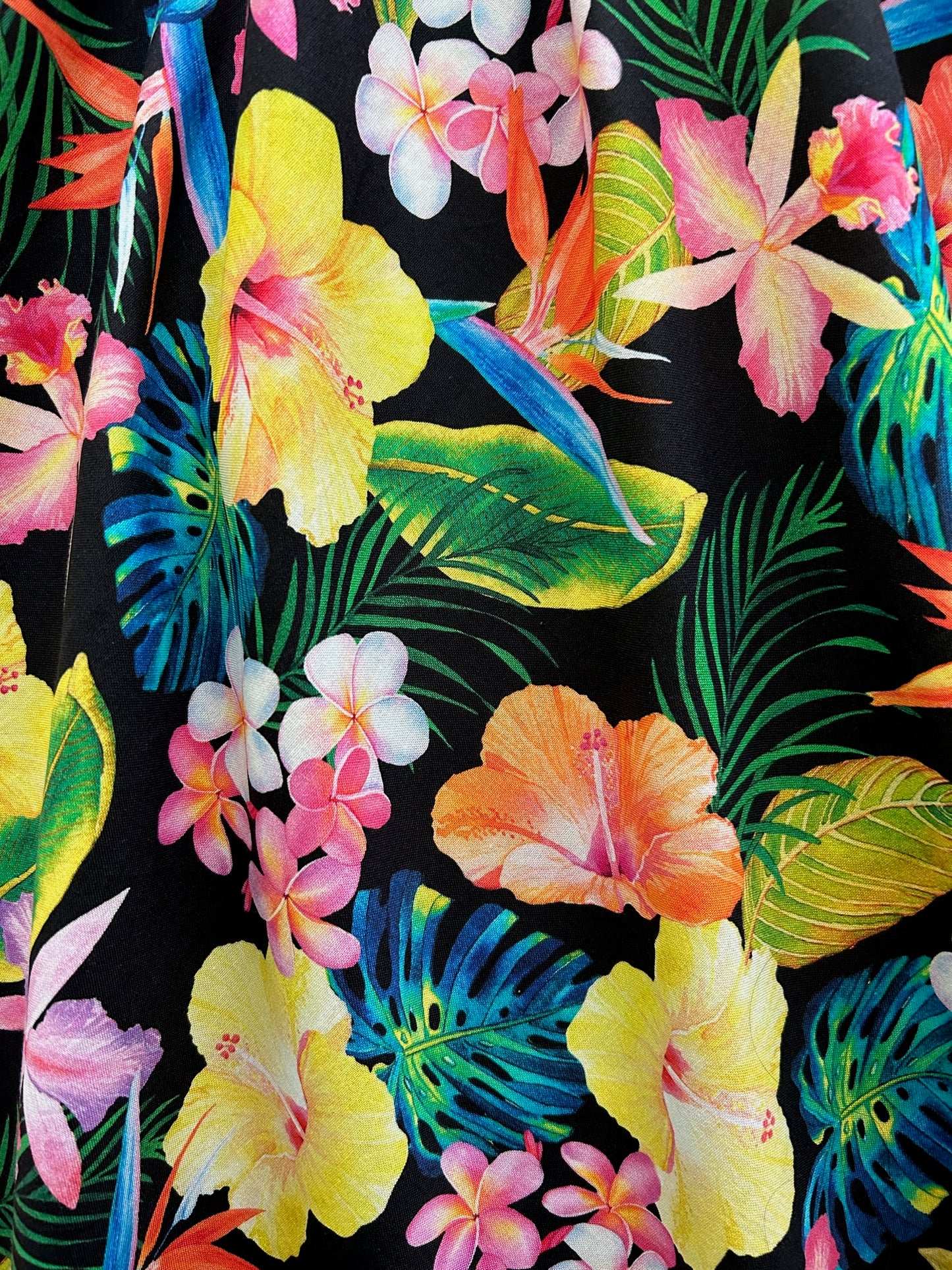 a close up of the fabric of tropical vintage dress showing tropical flowers on black background
