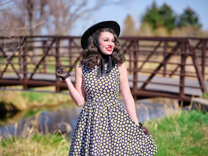 a close up image of model in front of a bridge wearing sunny side up vintage dress and a vintage hat
