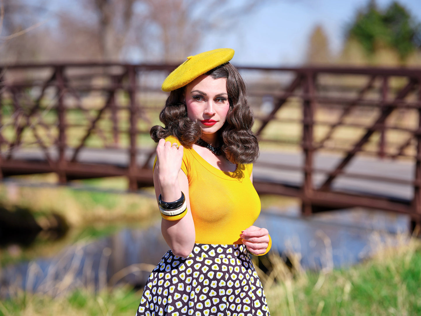a close up of a model standing outdoors in front of a bridge wearing the sunny side up skater skirt with mustard top and beret