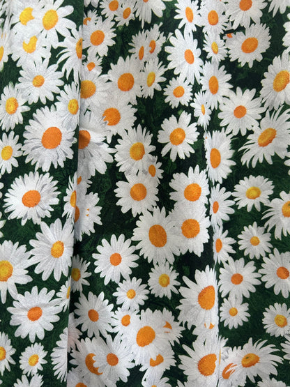 a close up of the fabric showing the packed daisies on dark green background
