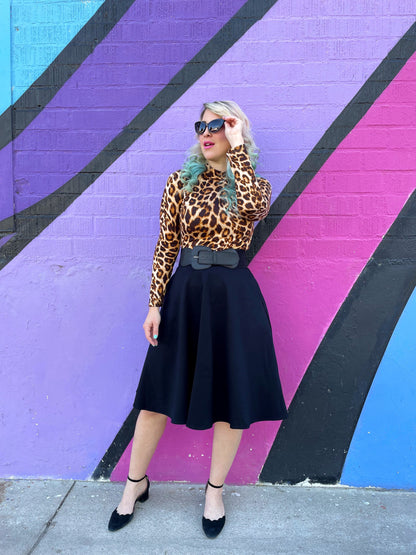 a full length of a model standing in front of a colorful wall wearing our leopard mock neck top