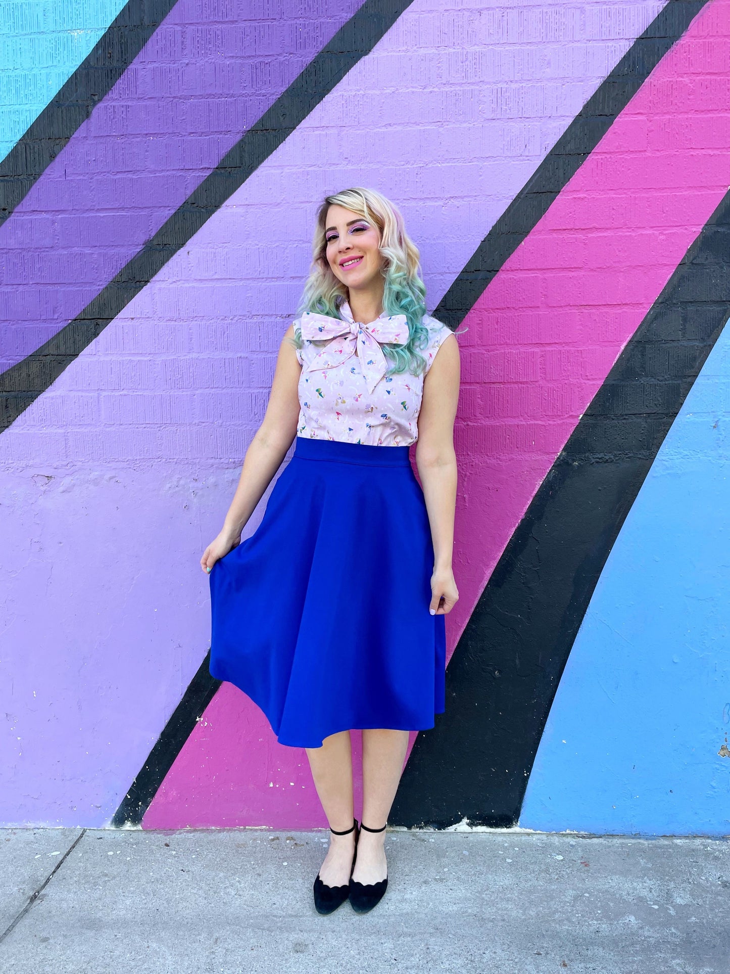 a model standing in front of pained wall wearing the charlotte skirt in royal blue