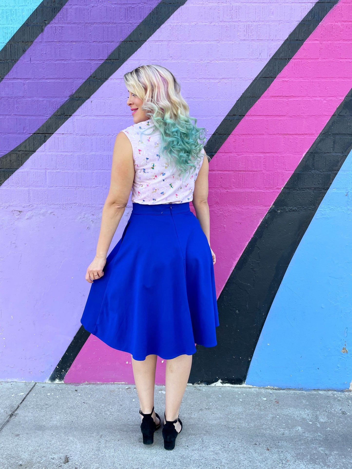 a back view of model standing in front of pained wall wearing the charlotte skirt in royal blue