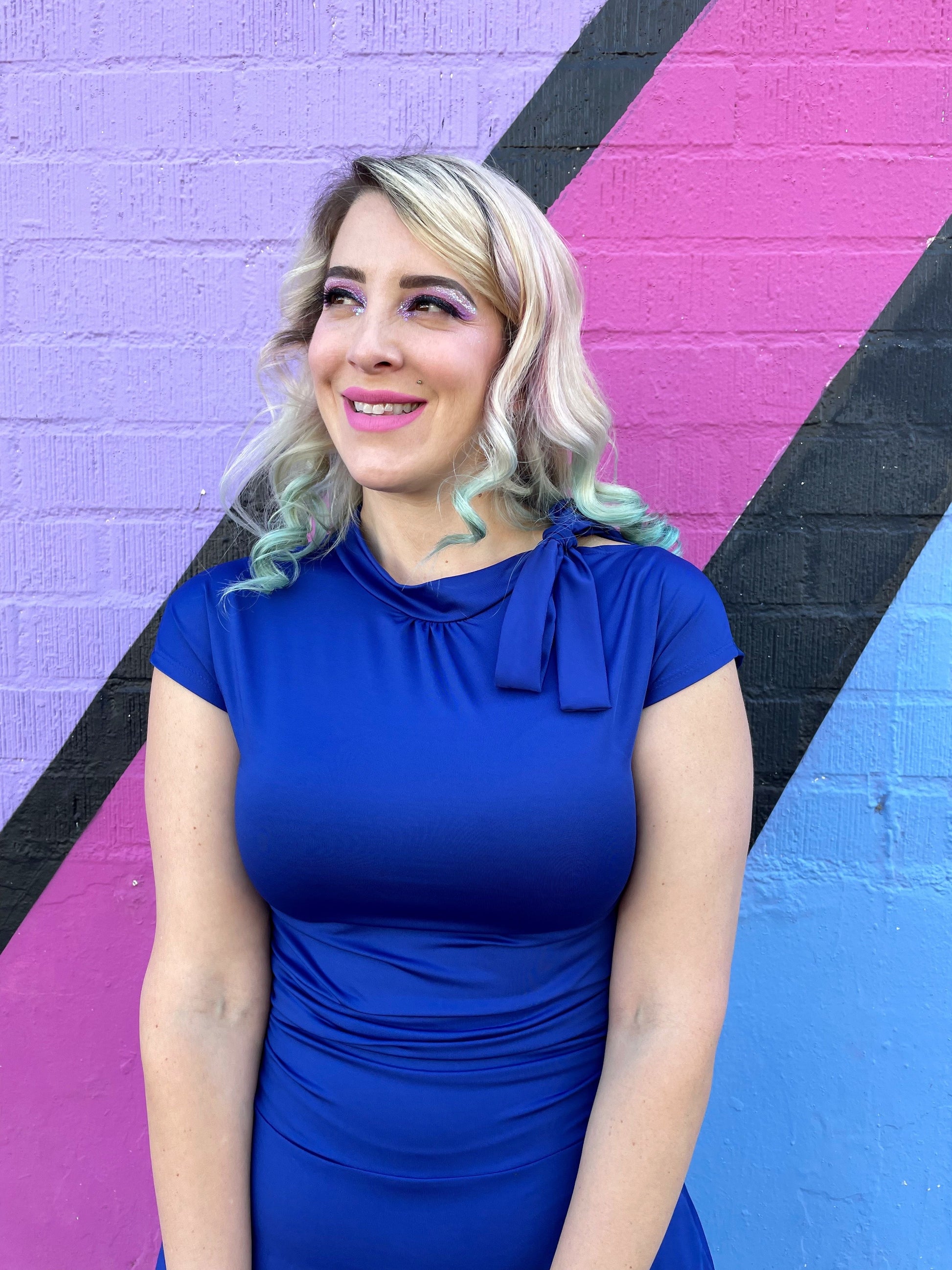 a close up of a model standing in front of a colorful wall wearing bombshell dress in royal blue