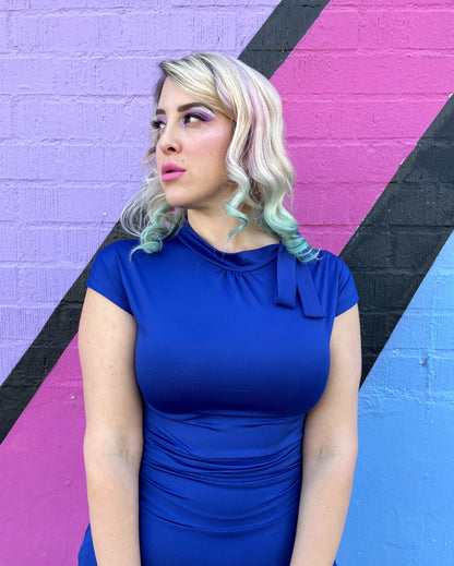 a close up of a model standing in front of a colorful wall wearing bombshell dress in royal blue