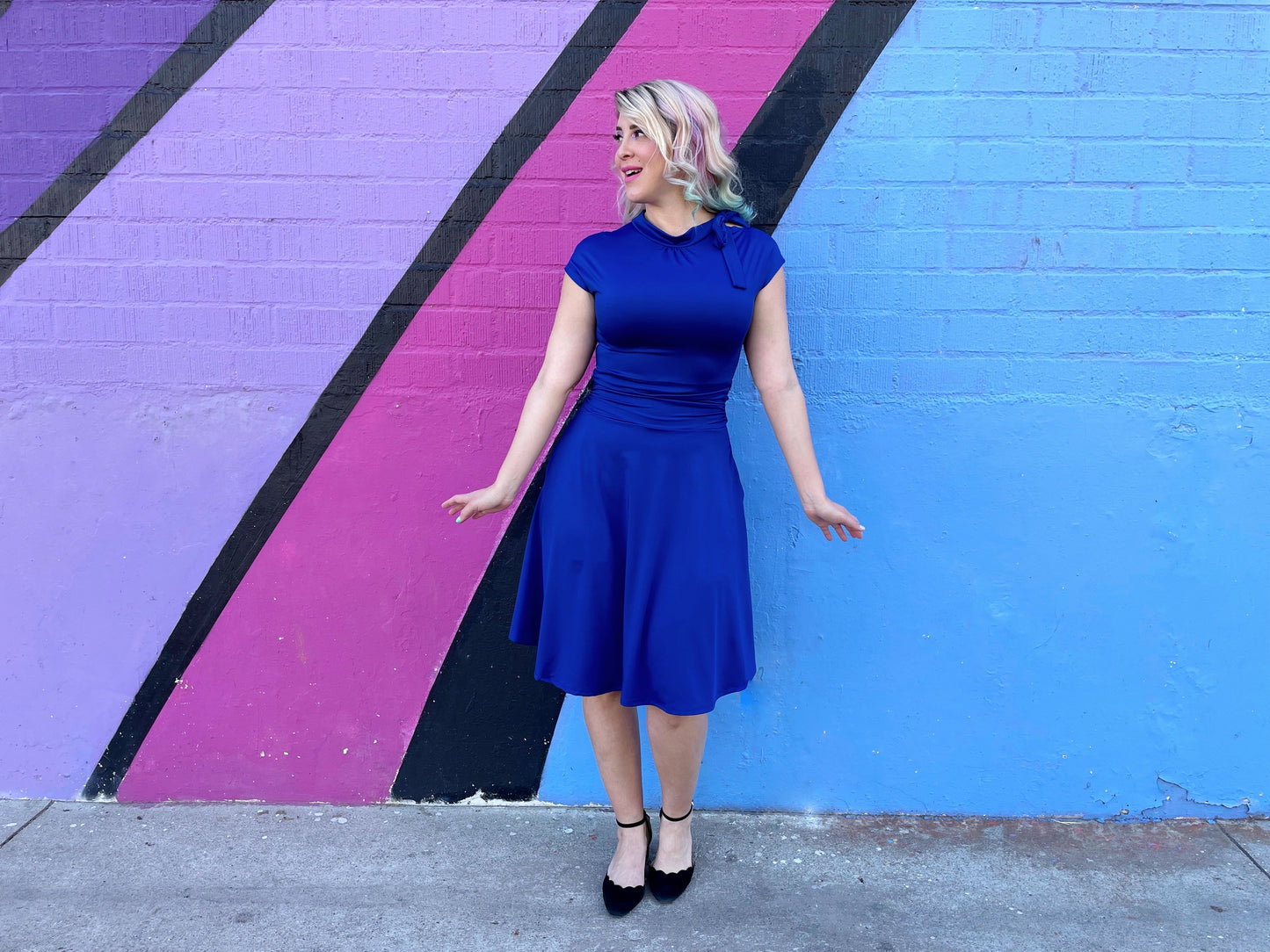 a full length of a model standing in front of a colorful wall wearing bombshell dress in royal blue