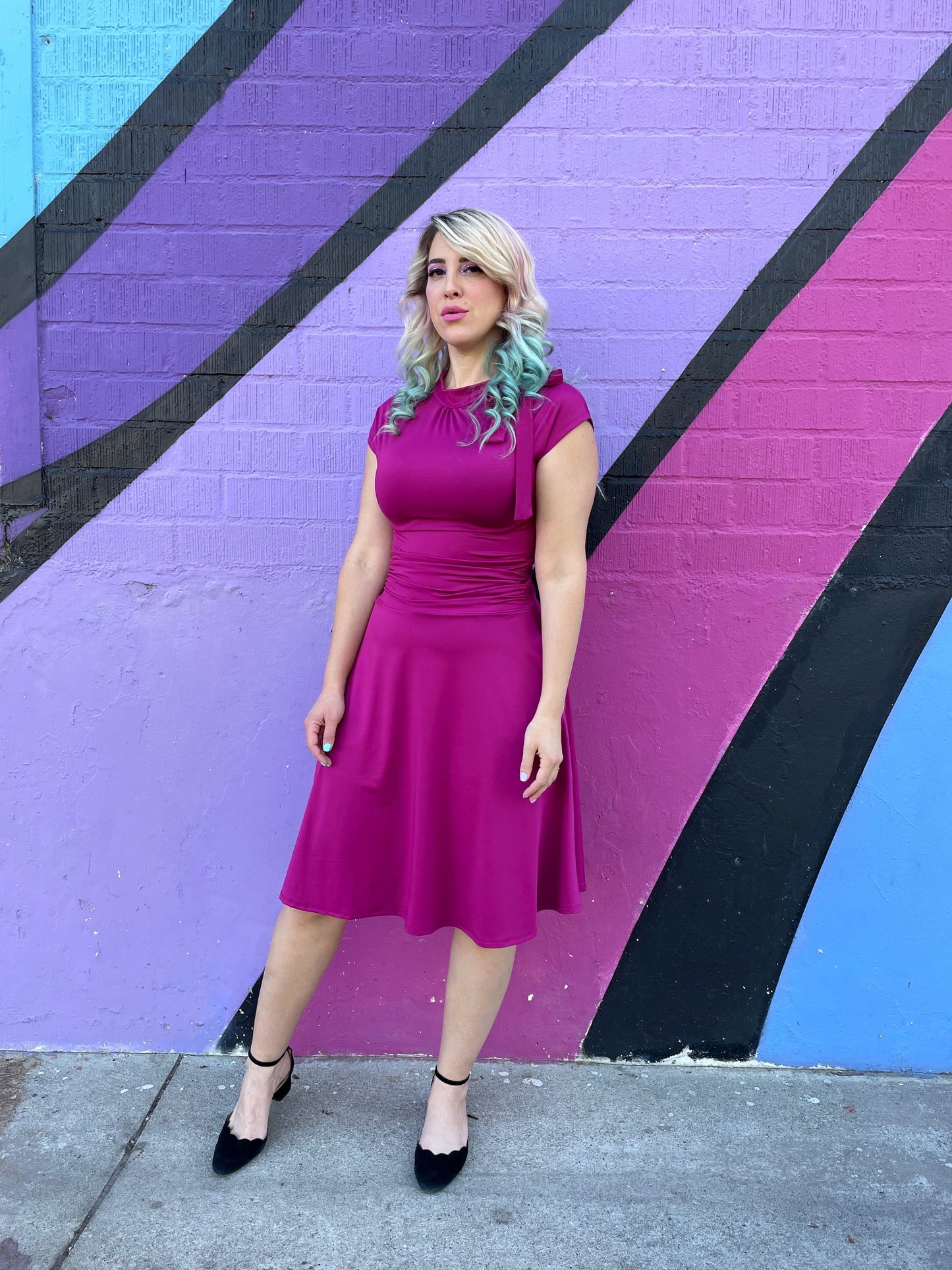 a full size of a model standing in front of a colorful wall wearing bombshell dress in magenta