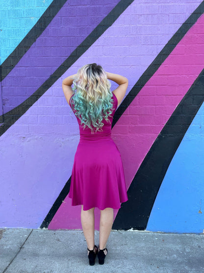 a full size of a backshot of a model standing in front of a colorfull wall wearing bombshell dress in magenta holding her hair up