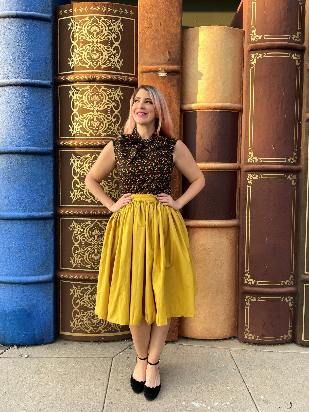 a full image of a model standing in front of books wearing peggy swing skirt in mustard she has her hands on her hips
