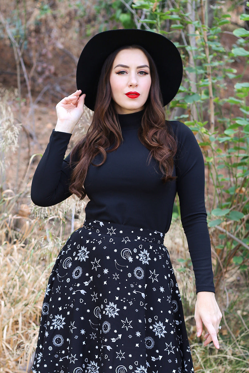 Model standing in the forest wearing a black stretch knit top with black skirt