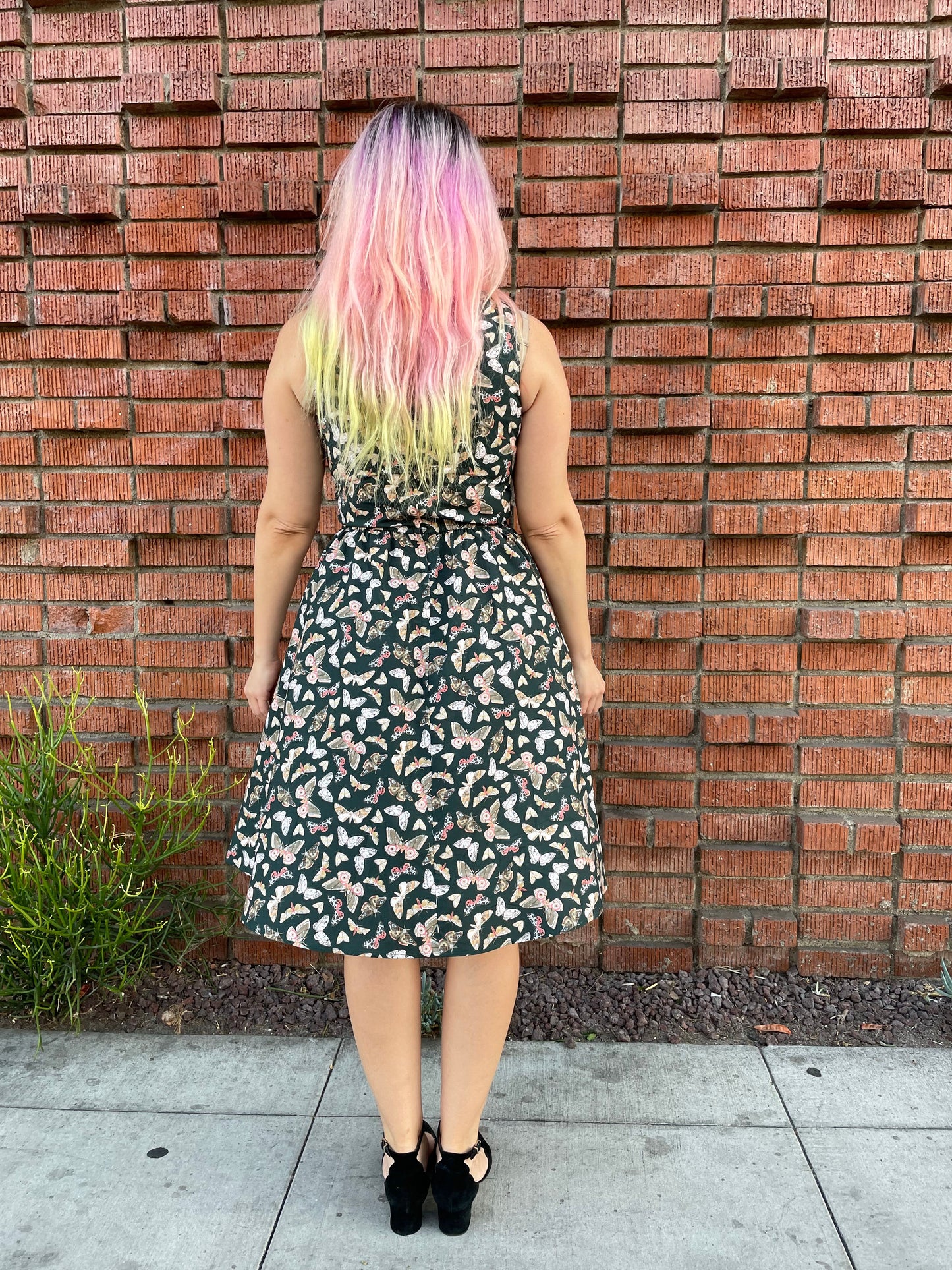 a full size image of the back of a model standing in front a brick wall wearing the butterfly vintage dress