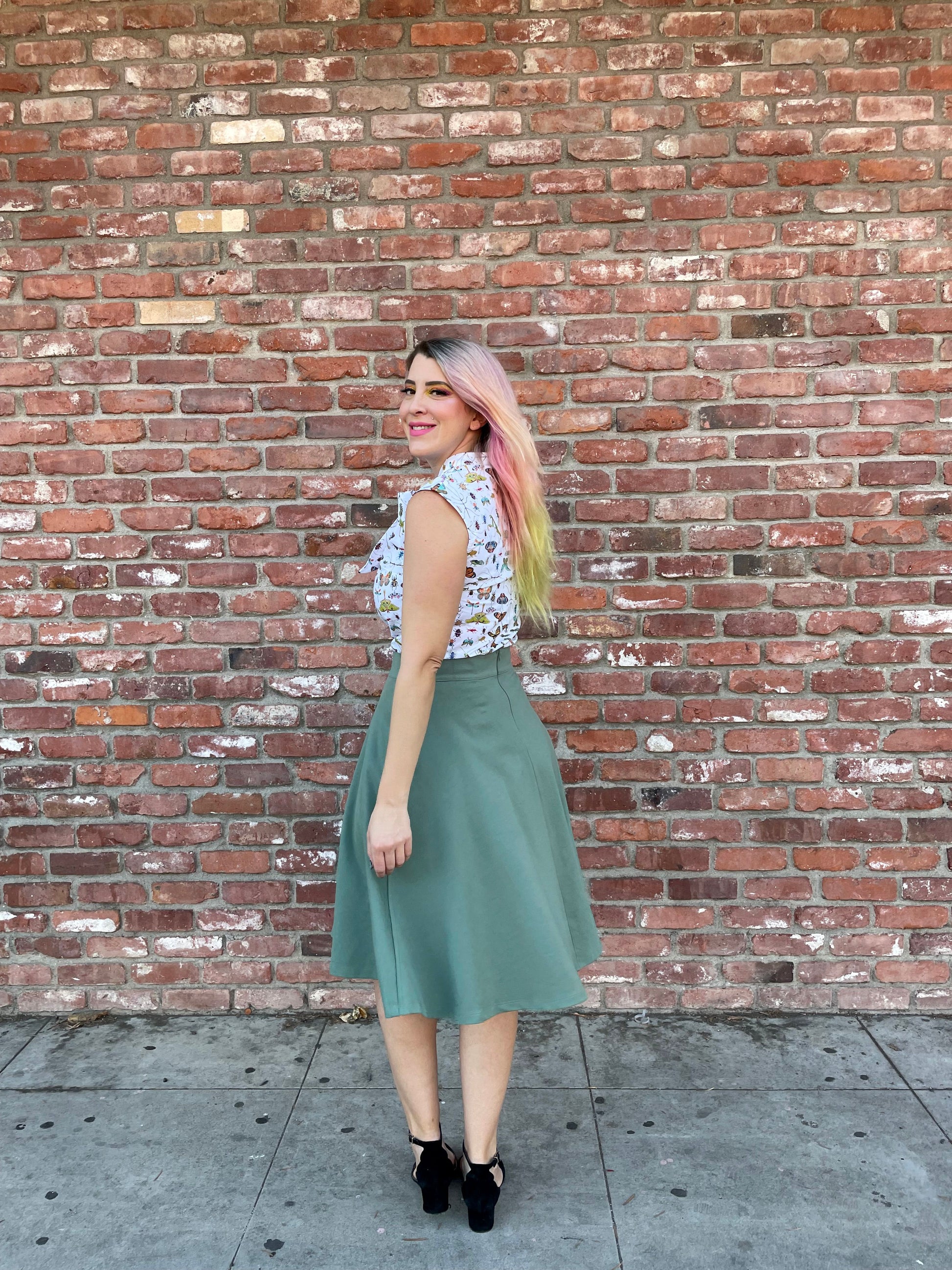 a full size image of a model standing in front of a brick wall wearing the charlotte skirt in sage 