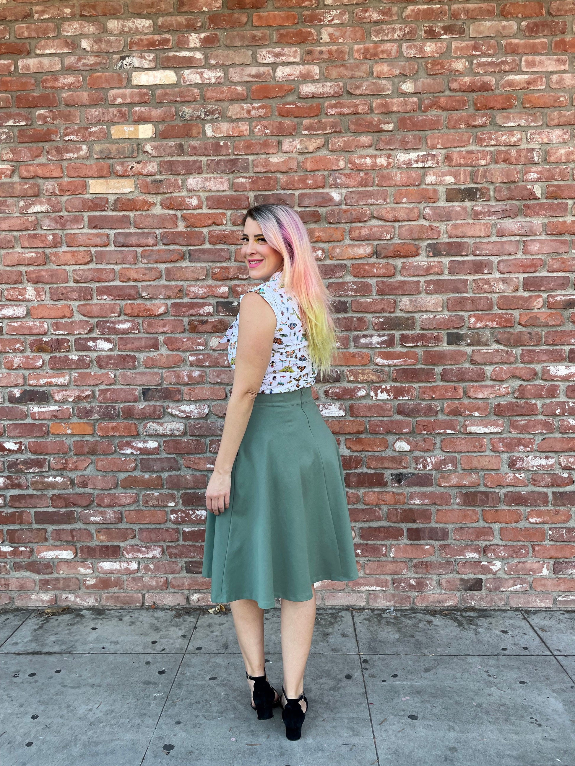 a full size image of a model standing in front of a brick wall wearing the charlotte skirt in sage 