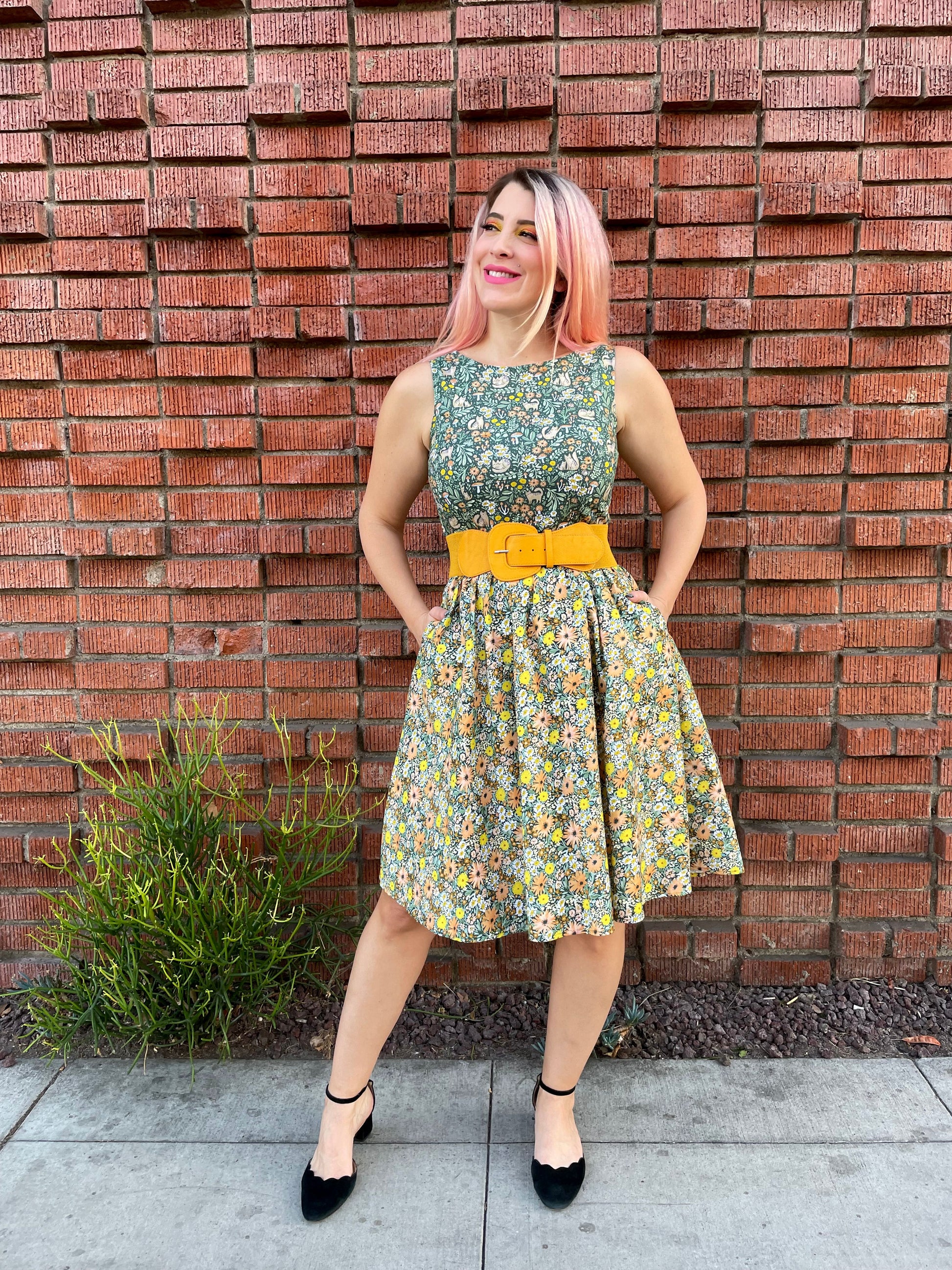 a full size image of a model standing in front of a brick wall wearing the cats in the fields twofer dress she has her hands in the pockets of the dress